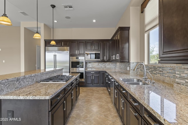 kitchen featuring light stone countertops, sink, backsplash, built in appliances, and pendant lighting