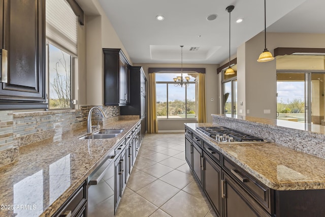 kitchen featuring light stone counters, stainless steel appliances, a tray ceiling, sink, and decorative light fixtures