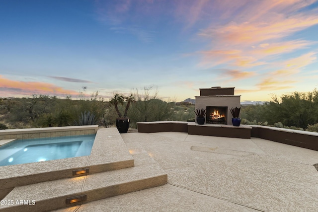 pool at dusk featuring a patio and exterior fireplace