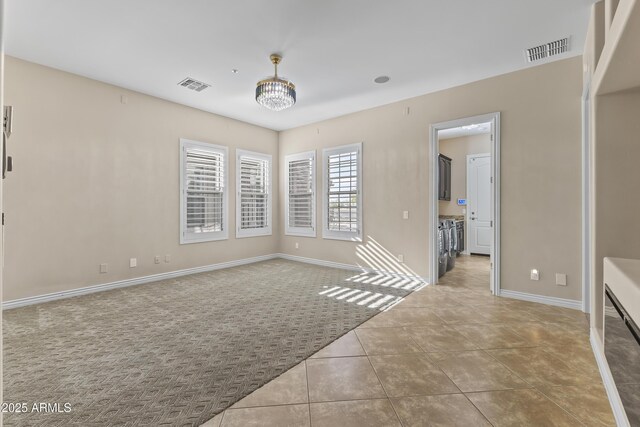 tiled empty room with a notable chandelier and washer and dryer