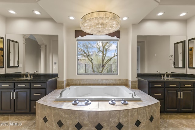 bathroom with a notable chandelier, vanity, ornate columns, and tiled bath