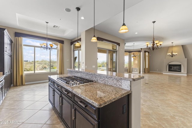 kitchen with light stone counters, a raised ceiling, pendant lighting, a fireplace, and stainless steel gas stovetop