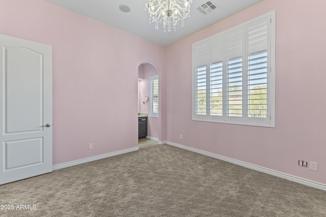 carpeted spare room featuring an inviting chandelier