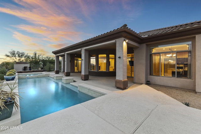 pool at dusk featuring a patio area and an in ground hot tub