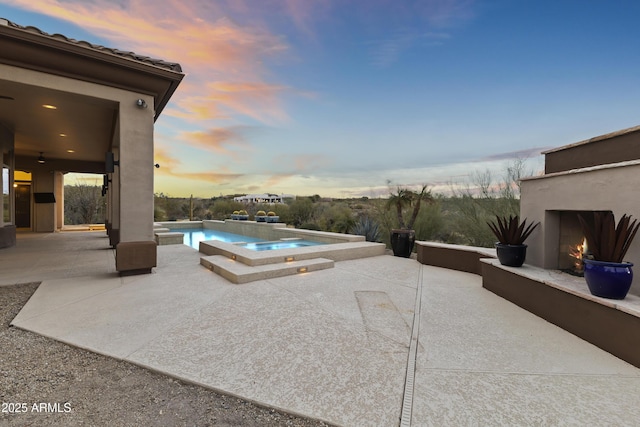 pool at dusk with a patio area, an in ground hot tub, and exterior fireplace