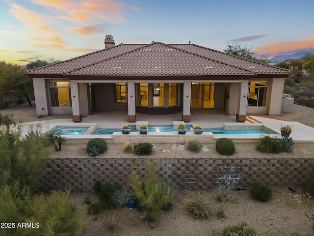 back house at dusk featuring an in ground hot tub and a patio area