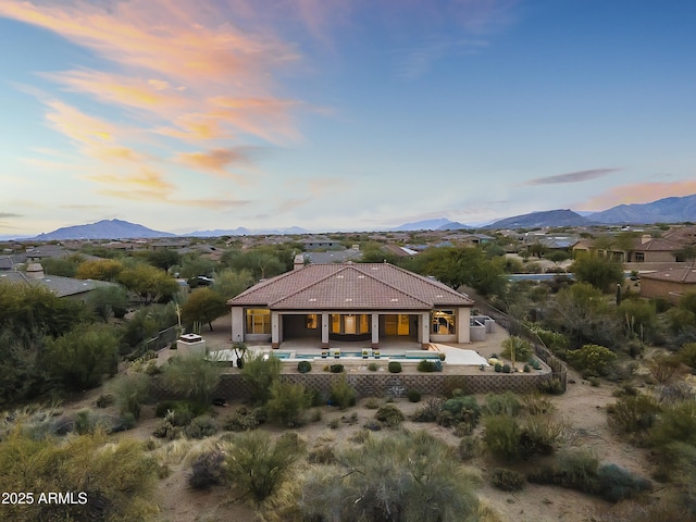 back house at dusk with a mountain view, a patio, and a pool