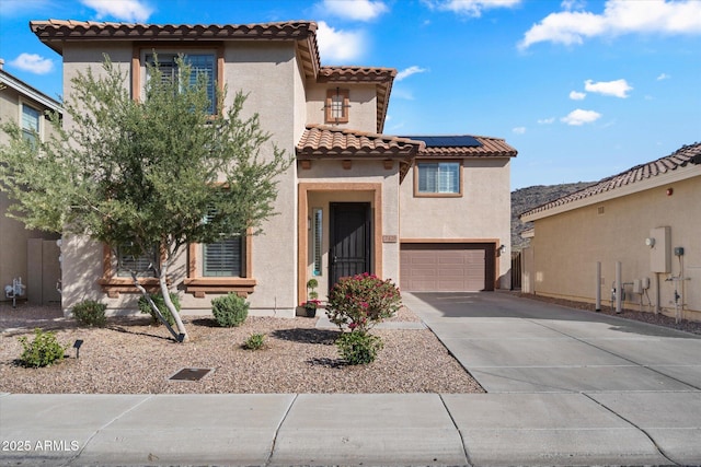 mediterranean / spanish house featuring stucco siding, driveway, a tile roof, an attached garage, and solar panels