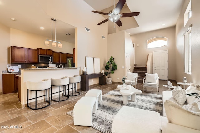 living room featuring stone tile floors, visible vents, a high ceiling, a ceiling fan, and stairs