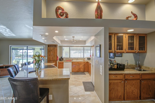 kitchen with light tile patterned flooring, sink, a kitchen bar, light stone countertops, and white appliances