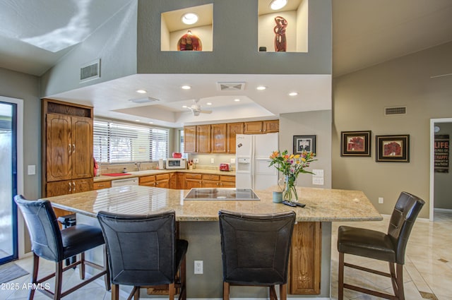 kitchen featuring sink, a breakfast bar area, light tile patterned floors, a tray ceiling, and white appliances