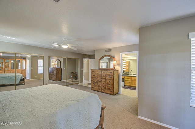 carpeted bedroom featuring connected bathroom, two closets, and ceiling fan