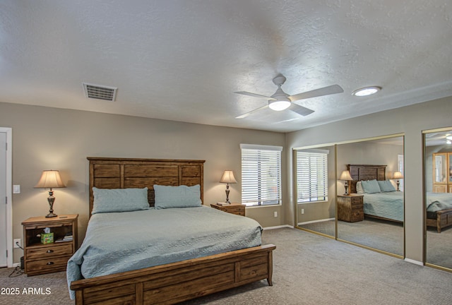 bedroom featuring ceiling fan, a textured ceiling, multiple closets, and carpet