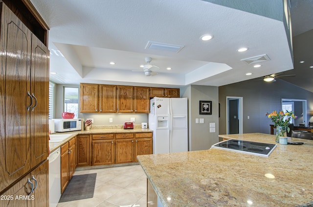 kitchen with a tray ceiling, light tile patterned floors, ceiling fan, light stone counters, and white appliances