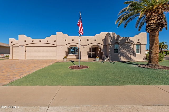 pueblo-style home featuring a garage and a front lawn