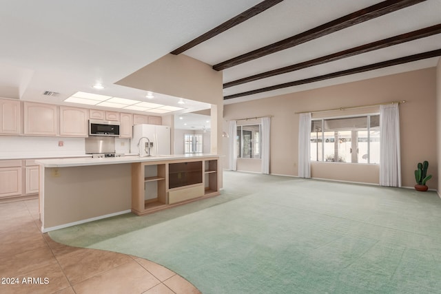 kitchen featuring beamed ceiling, a center island with sink, sink, white fridge with ice dispenser, and light colored carpet