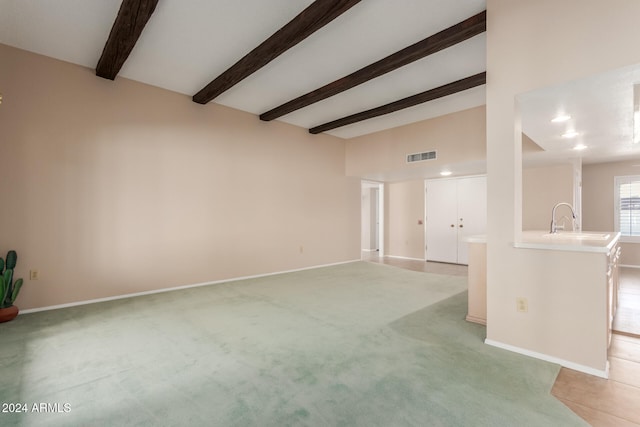 unfurnished living room with sink, light carpet, and beam ceiling