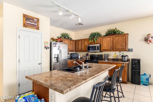 kitchen with a breakfast bar, an island with sink, sink, light tile patterned floors, and stainless steel appliances