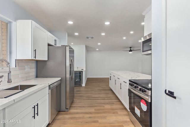 kitchen with light stone counters, white cabinets, appliances with stainless steel finishes, tasteful backsplash, and light wood-type flooring