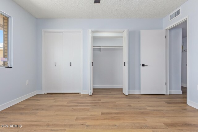 unfurnished bedroom with two closets, light hardwood / wood-style floors, and a textured ceiling