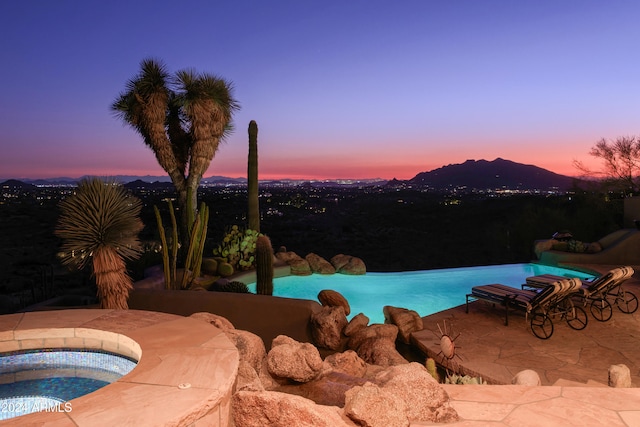 pool at dusk with an in ground hot tub and a patio area