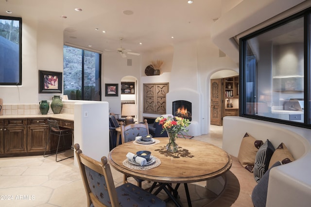 dining room featuring light tile patterned floors, a large fireplace, and ceiling fan