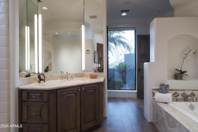 bathroom featuring vanity, a relaxing tiled tub, and hardwood / wood-style flooring