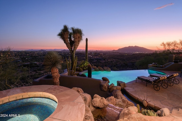 pool at dusk with an in ground hot tub, a mountain view, and a patio