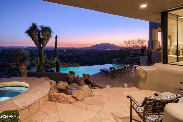 pool at dusk with an in ground hot tub, a patio area, and a mountain view