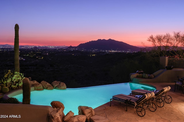 pool at dusk featuring a patio and a mountain view