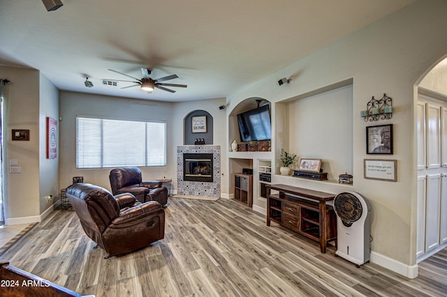 living room with wood-type flooring, built in features, ceiling fan, and a fireplace