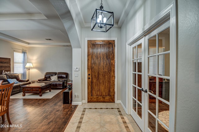 entrance foyer featuring a raised ceiling, ornamental molding, an inviting chandelier, and french doors