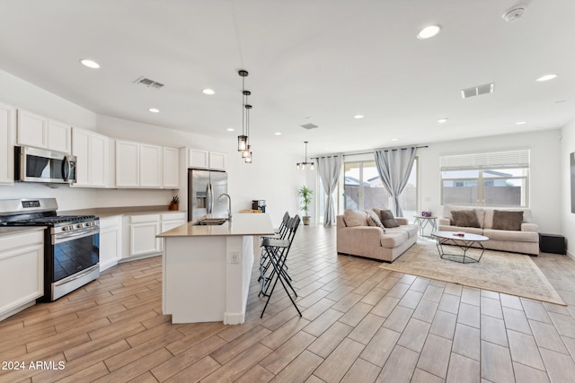 kitchen featuring a kitchen island with sink, appliances with stainless steel finishes, hanging light fixtures, and light hardwood / wood-style flooring