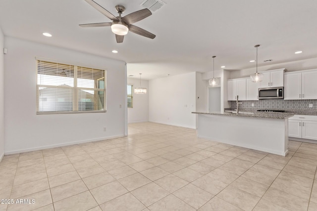 kitchen featuring tasteful backsplash, stainless steel microwave, visible vents, a ceiling fan, and light stone countertops