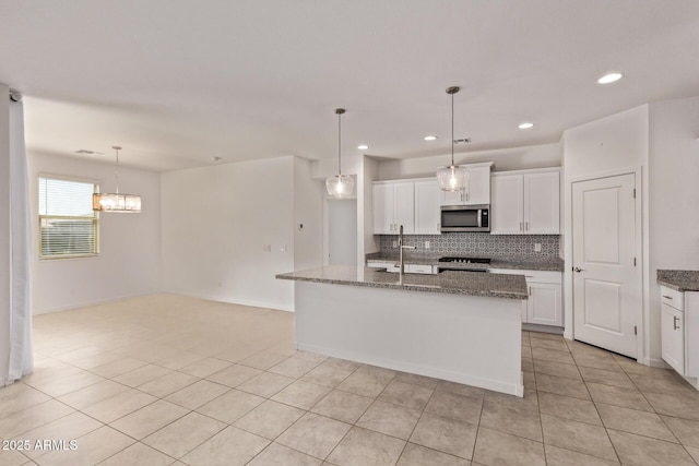 kitchen with light tile patterned floors, white cabinets, backsplash, range, and stainless steel microwave