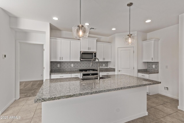 kitchen with light tile patterned floors, light stone countertops, stainless steel microwave, and white cabinetry