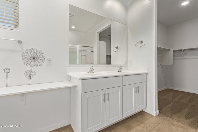 full bathroom with double vanity, a stall shower, tile patterned floors, a walk in closet, and a sink