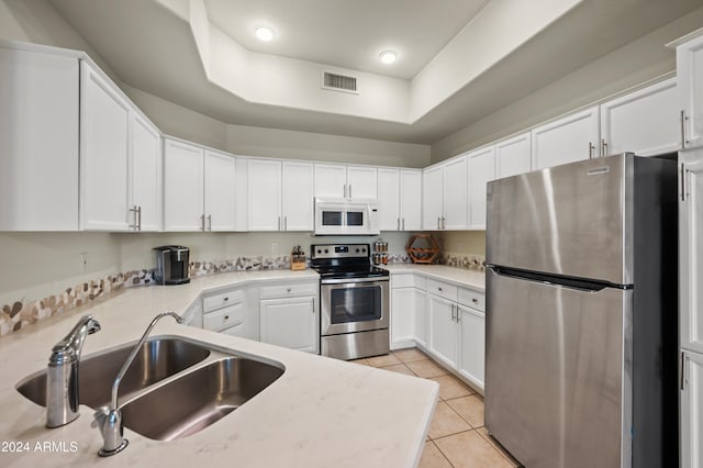 kitchen featuring sink, light tile patterned flooring, a tray ceiling, white cabinetry, and appliances with stainless steel finishes