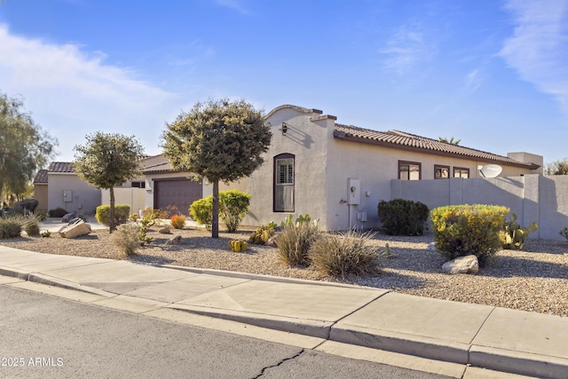 mediterranean / spanish house with a garage, fence, a tiled roof, and stucco siding