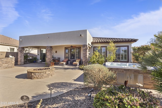 rear view of property with a hot tub, an outdoor fire pit, a ceiling fan, a patio, and stucco siding