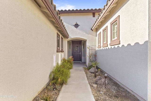 view of exterior entry with fence and stucco siding