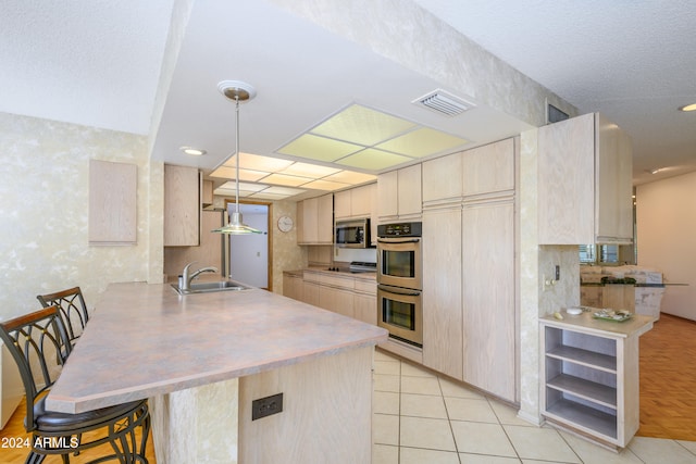 kitchen featuring kitchen peninsula, appliances with stainless steel finishes, light brown cabinetry, a breakfast bar, and sink