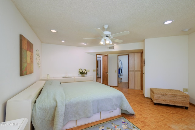 bedroom with a walk in closet, a textured ceiling, ceiling fan, light parquet flooring, and a closet