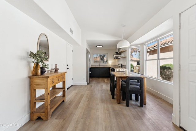 dining room featuring visible vents, baseboards, light wood-style floors, and vaulted ceiling