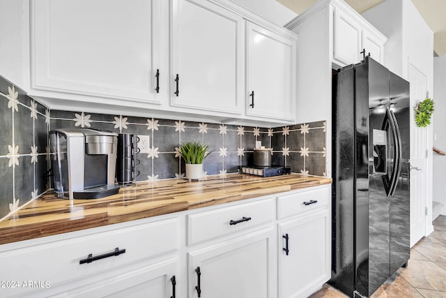 kitchen featuring white cabinetry, light tile patterned floors, wood counters, black fridge, and decorative backsplash