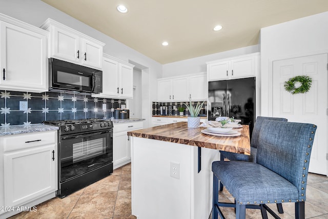 kitchen with black appliances, tasteful backsplash, a kitchen island, wood counters, and light tile patterned floors