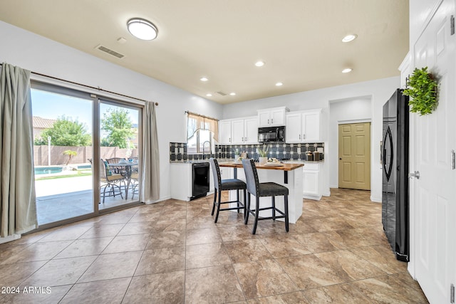 kitchen featuring black appliances, white cabinets, a kitchen island, light tile patterned floors, and backsplash