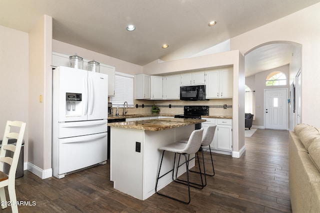 kitchen featuring white cabinets, a kitchen island, black appliances, dark stone counters, and vaulted ceiling