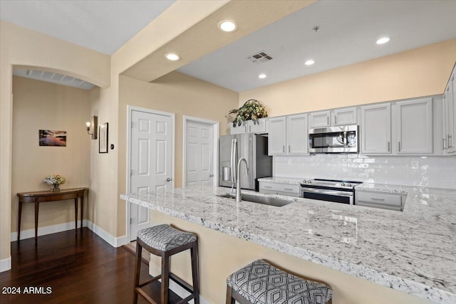 kitchen featuring sink, appliances with stainless steel finishes, light stone countertops, a kitchen bar, and dark hardwood / wood-style flooring