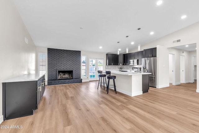 kitchen featuring decorative light fixtures, a breakfast bar area, a brick fireplace, a kitchen island with sink, and appliances with stainless steel finishes